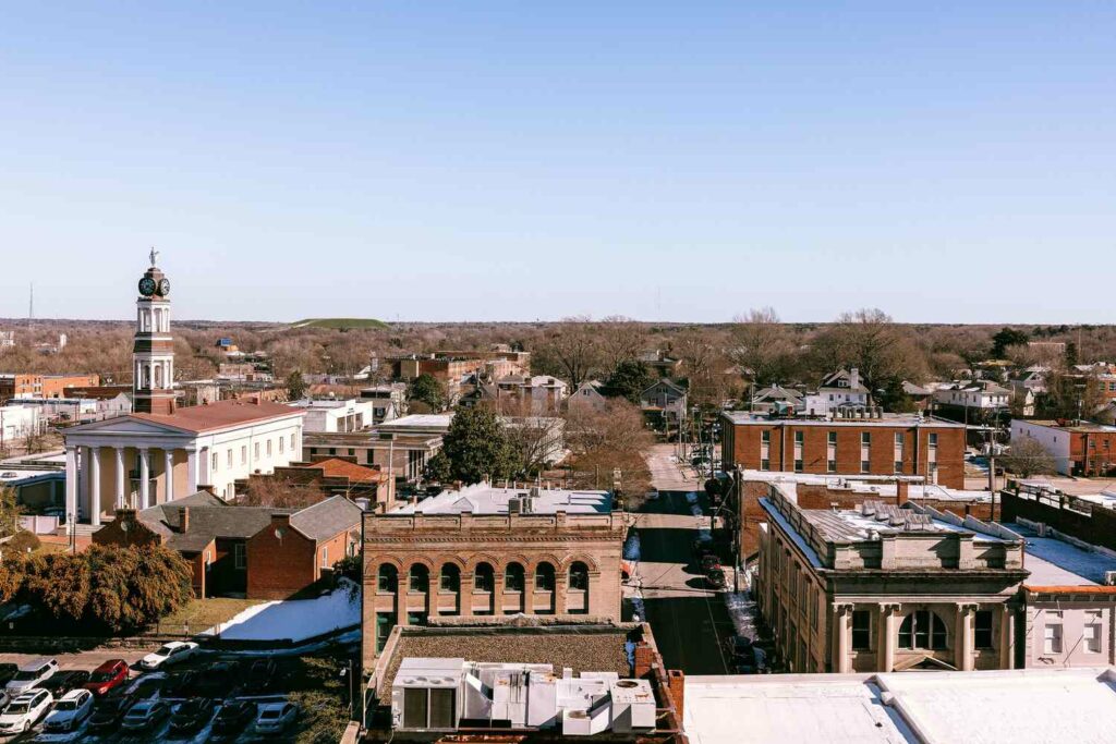 Aerial view of Charlottesville’s small town charm, with historic brick buildings, a courthouse featuring a clock tower, and parked cars under a clear blue sky.