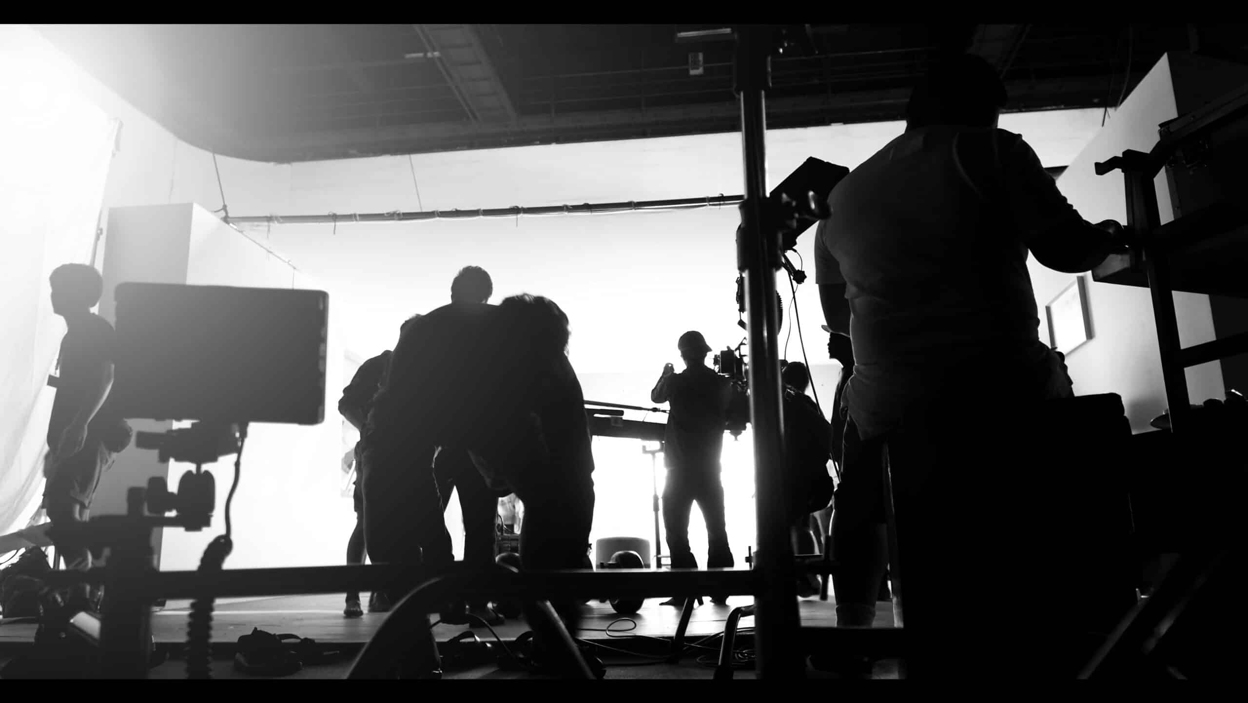 A group of people work on a film set, silhouetted against a bright background with various equipment visible, capturing the unexpected stories behind the magic of film production.